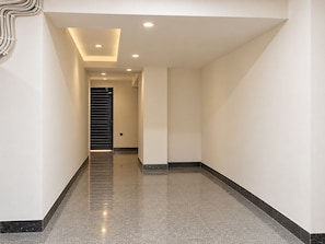 A modern hallway with a polished floor, recessed lighting, and a door at the end. - Mauryan Home Stay Near Yashobhoomi (New Delhi)