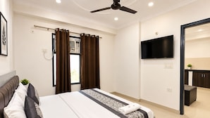 Un dormitorio moderno con cama, ventilador de techo, televisor y vistas a una zona de cocina.