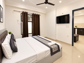 Une chambre moderne équipée d’un lit, d’un ventilateur de plafond, d’une télévision et offrant une vue sur un coin cuisine.