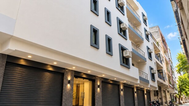 Un edificio de varios pisos con fachada blanca, varios balcones y una fila de persianas cerradas.