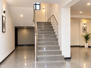 A modern interior with a staircase, polished stone flooring, and wall-mounted lighting. - Mauryan Home Stay Near Yashobhoomi (New Delhi)