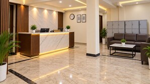 Zona de recepción de un hotel con un mostrador de mármol, un reloj y un área de descanso con un sofá y una mesa de centro.