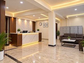 Un hall d’hôtel avec un comptoir de réception en marbre, une horloge et un espace détente comprenant un canapé et une table basse.
