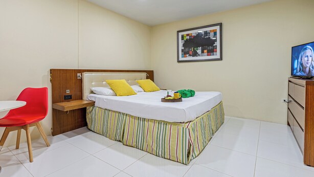 Ein Hotelzimmer mit einem Bett, einem Fernseher, einem roten Sessel und einem kleinen Tisch.