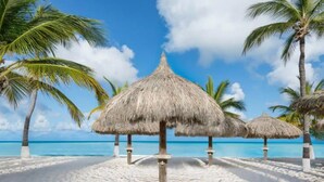 Ein Strand mit reetgedeckten Sonnenschirmen und Palmen.