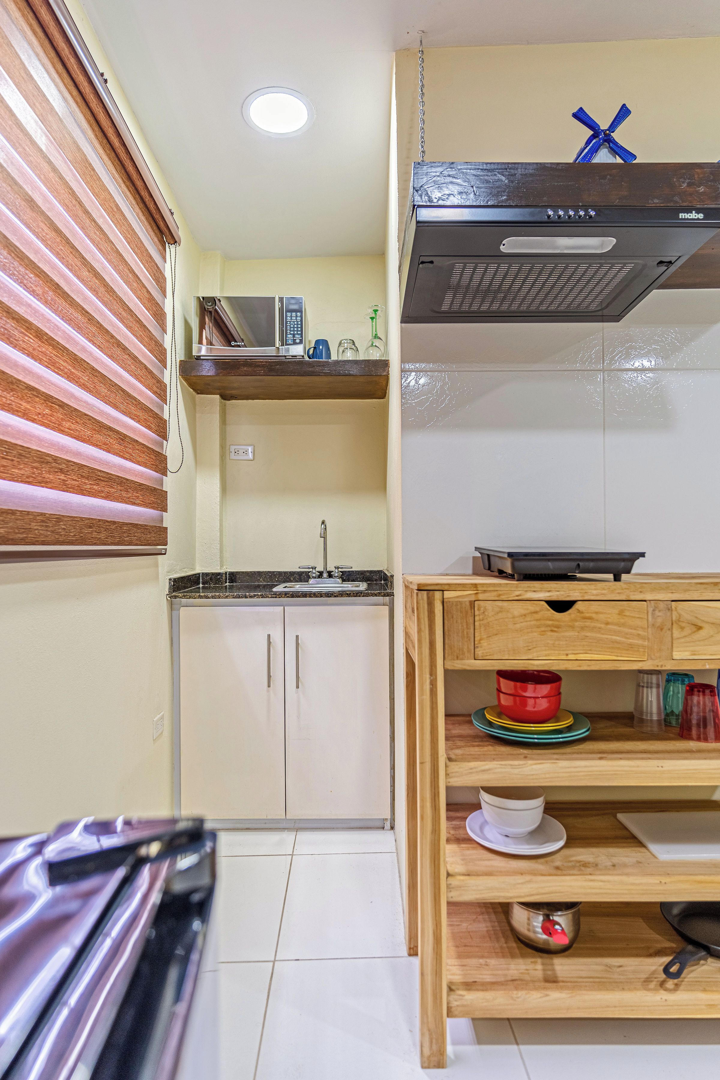 Cozinha compacta com micro-ondas, pia e mesa de madeira com louças.