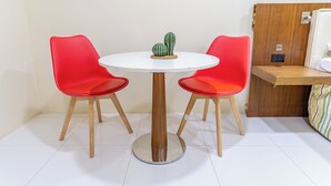 Ein kleiner runder Tisch mit zwei roten Stühlen, eine Kaktee auf dem Tisch und eine Holzkommode zur Rechten.