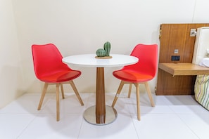 Une petite table ronde avec deux chaises rouges, un cactus posé sur la table et un meuble en bois sur la droite.
