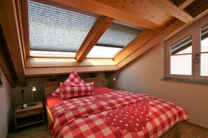 Quarto com claraboia, cama com roupa de cama vermelha, mesa de cabeceira e janela.