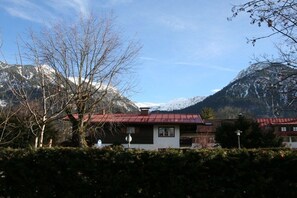 Uma cabana na montanha com telhado vermelho, rodeada por montanhas cobertas de neve e um céu claro.