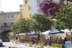 Un café al aire libre con mesas y sillas, un edificio de piedra con un letrero y un puente al fondo.