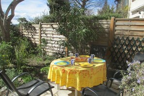 Un espacio de comedor al aire libre con una mesa preparada para cuatro personas, rodeado de sillas.