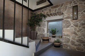 Un intérieur avec un mur en pierre, une fenêtre, des plantes en pot et un escalier.