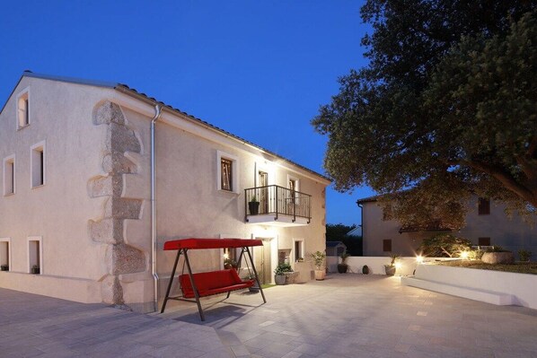 A two-story building with a balcony, a swing set, and a paved courtyard. - Villa in Kornic, Krk with swimming pool (Kornic, Krk)
