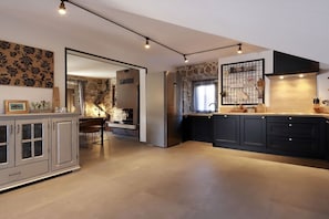 Une cuisine moderne avec un mur d’accent en pierre, un four encastré et un grand îlot central doté de meubles de rangement aux couleurs foncées.