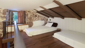 Een slaapkamer met een stenen muur, houten balken, een raam met gordijnen en twee bedden.