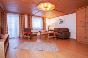Ein gemütliches Wohnzimmer mit Holzboden, einem Sofa, einem Sessel, einem Tisch und einem Schrank.