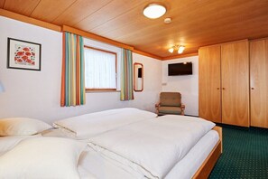 Ein Schlafzimmer mit zwei Betten, einem Sessel, einem Fernseher und Holzschränken.