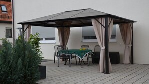 Un patio cubierto con una mesa y sillas, una planta en maceta y un edificio al fondo.