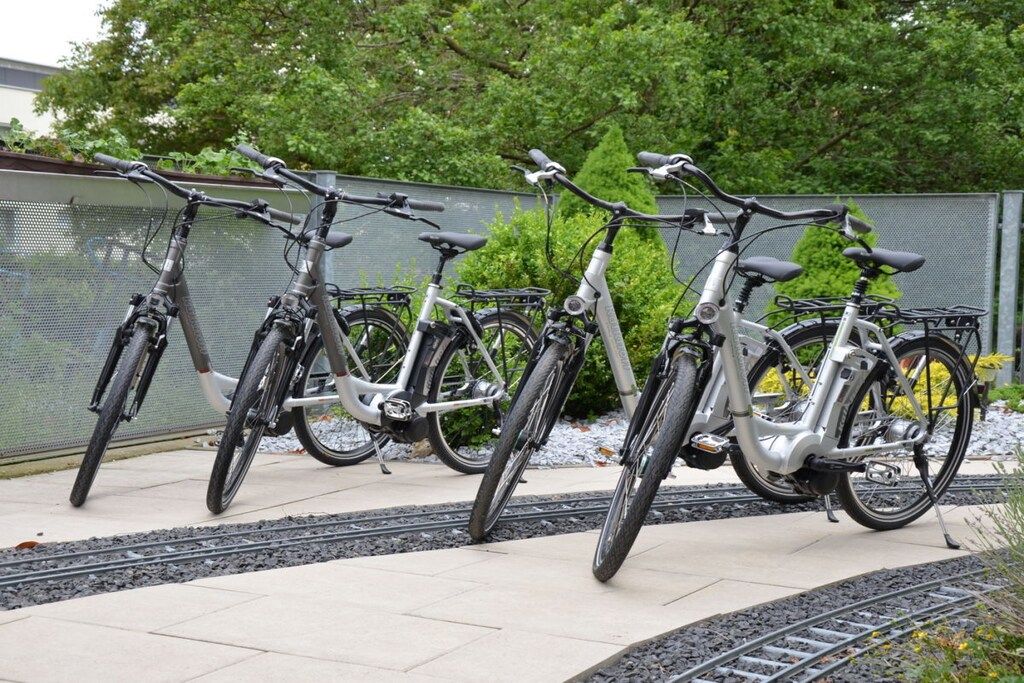 Een rij fietsen geparkeerd op een verharde ondergrond, naast een hek.