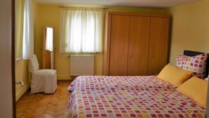 Un dormitorio con cama, una silla, un armario y una ventana con cortinas.