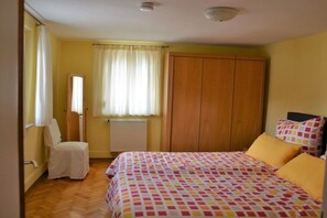 Ein Schlafzimmer mit einem Bett, einem Sessel, einem Kleiderschrank und einem Fenster mit Vorhängen.
