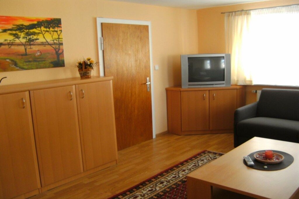 Een woonkamer met een televisie op een houten kast, een bank en een eettafel, met een afstandsbediening.