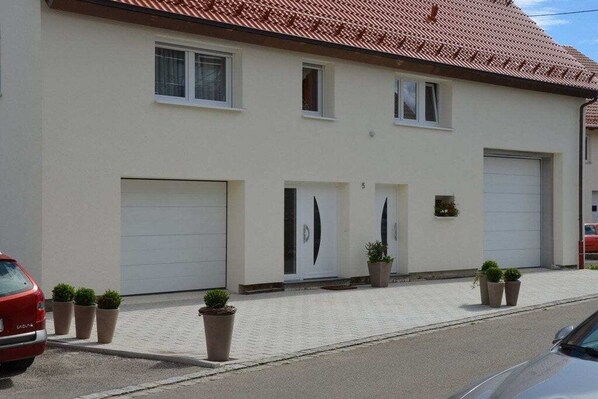 Ein zweistöckiges Gebäude mit Garage im Erdgeschoss und einer Auffahrt mit Kübelpflanzen.