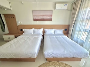 Habitación de hotel con dos camas individuales, cabecera de madera, aire acondicionado instalado en la pared y ventana con cortinas.