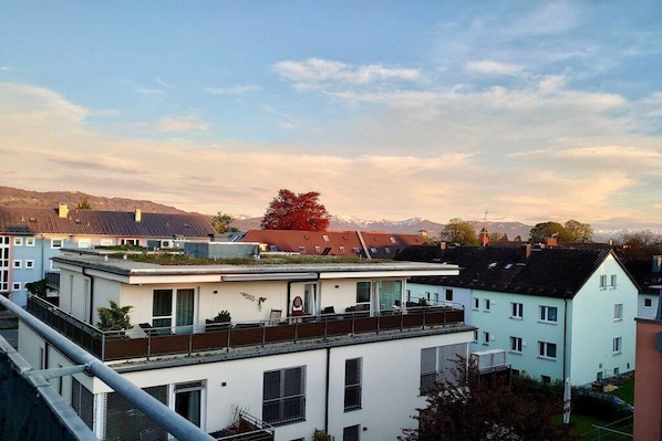 Zona residencial com edifícios modernos, uma construção com telhado plano e vista para montanhas ao longe.