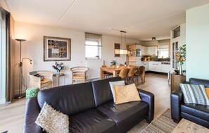 A modern living room with a black leather sofa, a dining area with a wooden table, and a kitchen with white cabinets. - Nice home in Stevensweert with WiFi (Stevensweert)