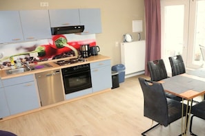 A compact kitchen with a dishwasher, oven, and coffee maker. There is a dining area with a table and chairs. - Becker Holiday Winery Apartment "Hasenläufer" (Burgen)