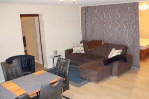 A living room with a sofa, a dining table with chairs, and a patterned curtain. - Becker Holiday Winery Apartment "Hasenläufer" (Burgen)