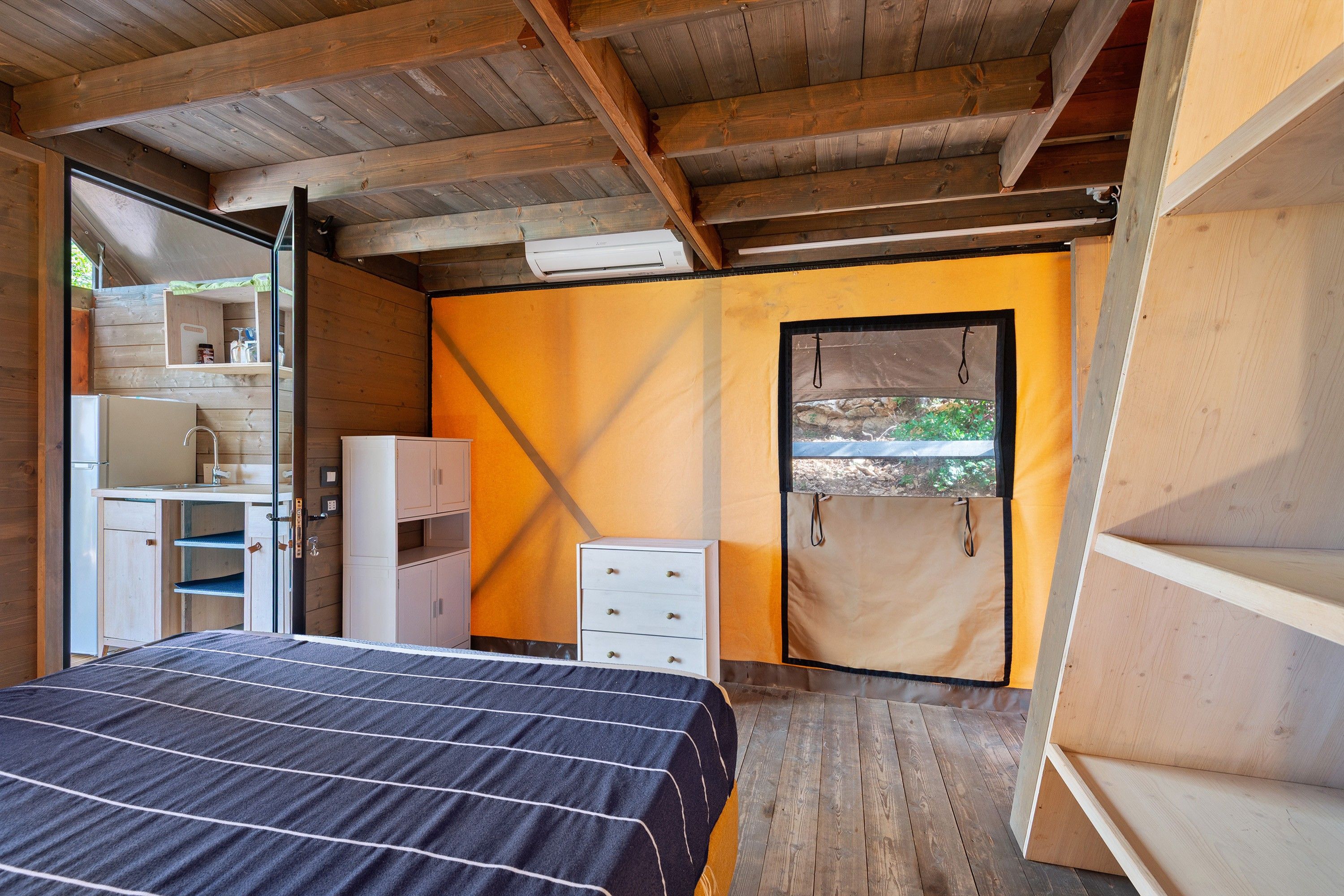 A bedroom with a bed, a wardrobe, a dresser, and a window with a view of greenery.