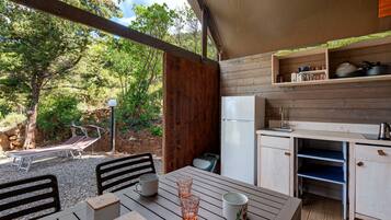Une cabane en bois comprenant une table à manger, des chaises, un réfrigérateur et un petit coin cuisine avec des étagères.