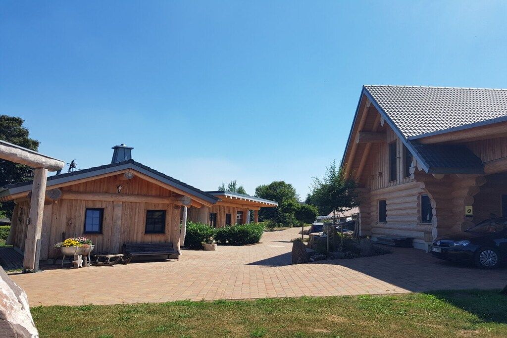 Een houten chalet met een overdekte veranda, een geplaveid pad en een geparkeerde auto in de buurt.