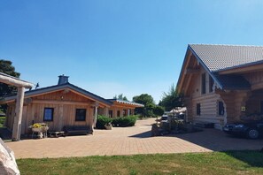 Een houten chalet met een overdekte veranda, een geplaveid pad en een geparkeerde auto in de buurt.