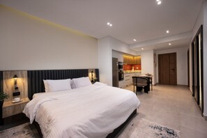 A modern hotel room with a large bed, a small kitchenette, and a separate dining area.