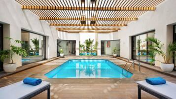 Une piscine intérieure moderne avec un plafond en bois, des chaises longues et des plantes en pot.