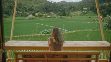 A person sitting on a wooden bench with a view of a green field and distant houses.