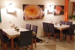 Et spiseområde med to borde, stole, vægmonteret lys og blomsterkunst.