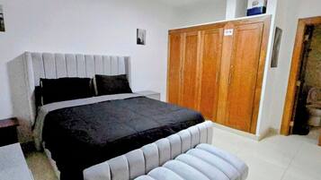 Um quarto com cama, um banco, guarda-roupa e secretária.