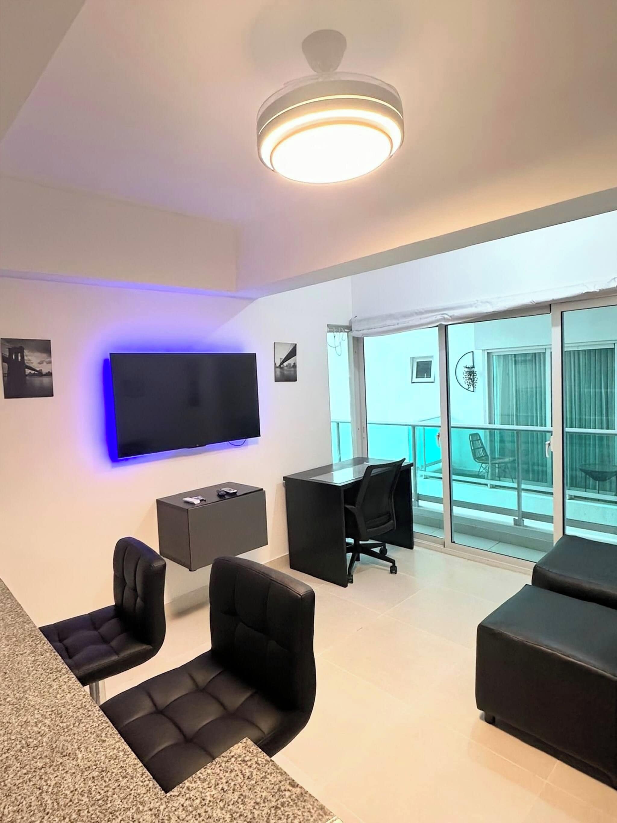 Uma sala de estar moderna com televisão de tela plana, luminária no teto e varanda com portas de vidro.