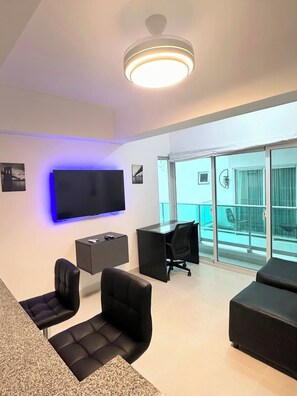 Un salon moderne doté d’un téléviseur à écran plat, d’un luminaire au plafond et d’un balcon avec des portes vitrées.