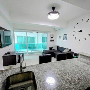 A modern living room with a kitchen area, a large window, and a wall clock. - Feel at Homewith Best View in the City Pool (Santo Domingo)