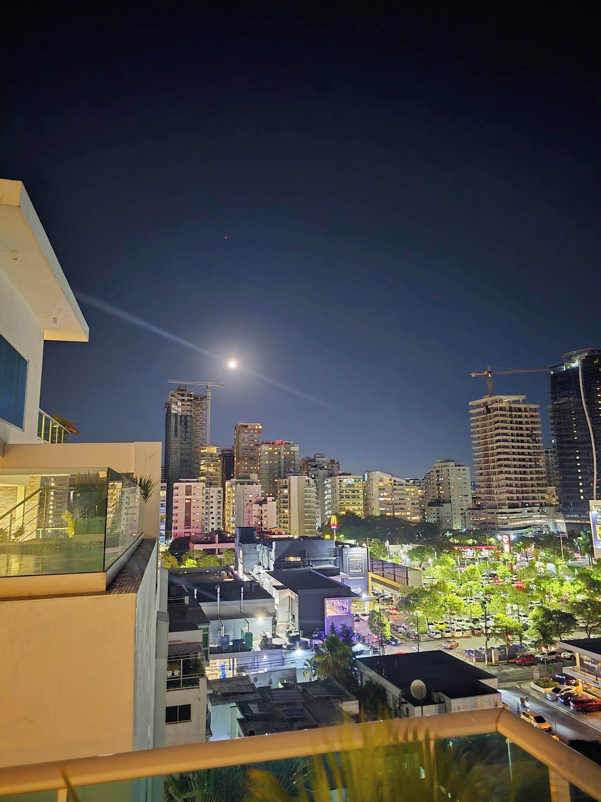 Paisagem urbana noturna com um edifício imponente, fachada de vidro e terraço no telhado.