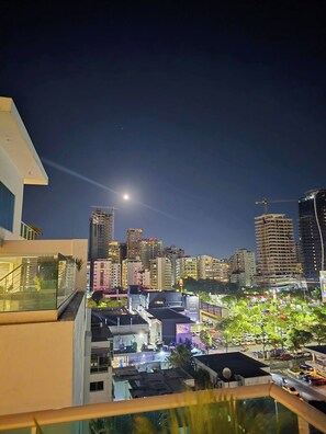 Paisagem urbana noturna com um edifício imponente, fachada de vidro e terraço no telhado.