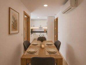 Un comedor con una mesa de madera dispuesta para cuatro personas, sillas y un florero con vela.