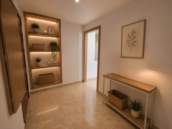 A hallway with a wooden console table, shelves with plants and baskets, and a framed artwork on the wall.