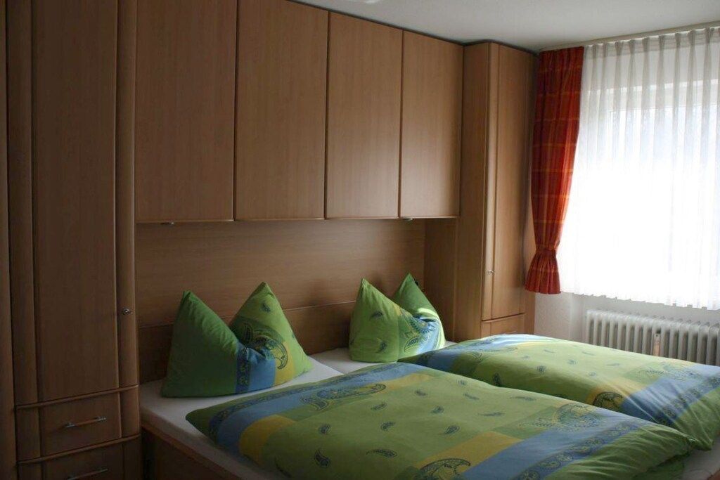 A bedroom with a wooden headboard, two beds with green and blue bedding, and a window with a red curtain.
